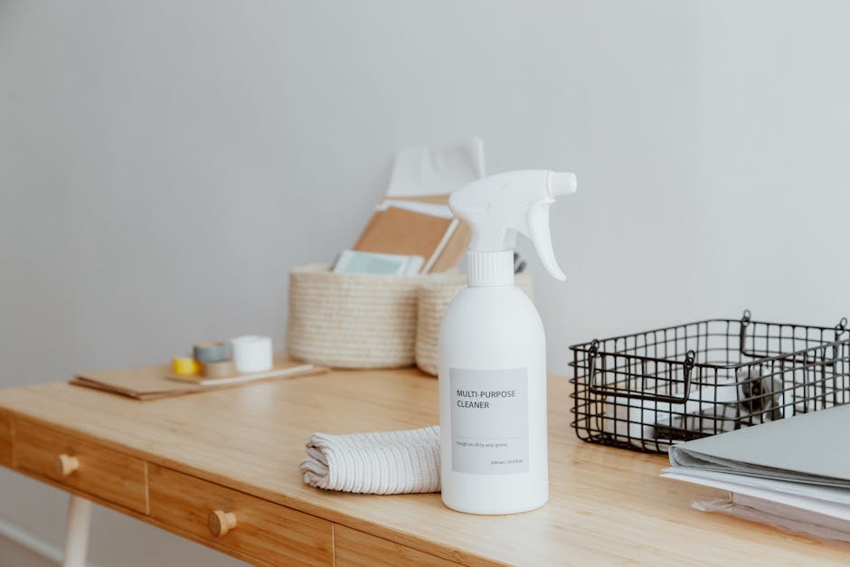 A person wearing pink rubber cleaning gloves holding a blue spray bottle filled with cleaning solution, standing in front of a white marble or quartz countertop. The surface appears clean and smooth, 
